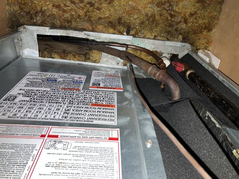 Completed planned furnace maintenance inspection on residential HVAC system. Performed comprehensive visual inspection of unit exterior, verified all manufacturer labels and safety instructions were intact and legible, and examined refrigerant line connections at unit base for proper installation and signs of wear. Inspected interior components including copper refrigerant lines, red valve assembly, and associated piping for corrosion, oxidation, and operational integrity. All components found to be functioning within normal parameters with age-appropriate patina on copper lines. Unit operational and ready for continued service.