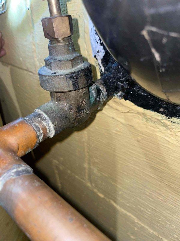 Responded to basement water leak complaint and performed diagnostic inspection of plumbing system. Located active leak at aged brass valve assembly connected to copper piping near water heater. Valve body showed significant corrosion and deterioration at threaded connections, with visible oxidation on copper supply lines. Inspected surrounding plumbing infrastructure including horizontal copper runs, PVC drainage system, and shut-off valves to assess overall system condition and identify source of leak. Documented plumbing configuration and leak location with photographs for repair recommendations.