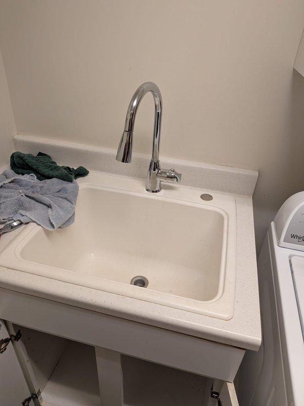 Responded to service call for leaking laundry tub faucet at base. Removed and disposed of old faucet assembly, then installed customer-supplied chrome pull-down faucet with gooseneck spout. Connected hot and cold water supply lines using braided flexible hoses, secured all connections, and tested for proper operation and leaks. System functioning properly upon completion.