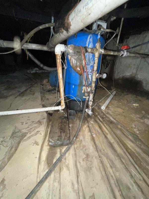 Responded to water leak in crawlspace on main inlet line from well pump to house. Upon arrival, inspected blue pressure tank and associated plumbing connections in confined crawlspace area. Located active leak on main inlet piping near pressure tank assembly. Equipment showed significant age and corrosion, with weathered blue pressure tank, corroded fittings, and deteriorated pipe connections. Documented leak location and condition of existing plumbing system including copper piping, PVC connections, and flexible hoses. Advised customer of repair requirements for inlet line and recommended water shutoff to prevent further water damage until permanent repairs could be completed.