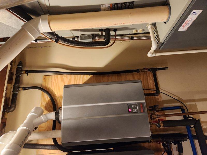 Responded to service call for tankless water heater experiencing constant beeping and displaying temperature-related error code. Upon arrival, accessed utility room via side door adjacent to garage. Performed diagnostic evaluation of dual tankless water heater system mounted in mechanical space. Inspected control panels, digital displays, and error code indicators on both units. Verified no active water leaks present at copper piping connections, PVC venting, or shut-off valves. Examined plumbing connections including blue-handled isolation valves and associated copper supply lines. Assessed venting system integrity including white PVC intake/exhaust pipes. Reviewed system wiring and electrical connections to units. Documented equipment condition through photographic records showing installation configuration, control panel status, and plumbing connections. Identified error code related to water temperature sensor or heating element malfunction preventing unit operation. Provided diagn