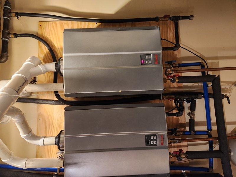 Responded to service call for tankless water heater experiencing constant beeping and displaying temperature-related error code. Upon arrival, accessed utility room via side door adjacent to garage. Performed diagnostic evaluation of dual tankless water heater system mounted in mechanical space. Inspected control panels, digital displays, and error code indicators on both units. Verified no active water leaks present at copper piping connections, PVC venting, or shut-off valves. Examined plumbing connections including blue-handled isolation valves and associated copper supply lines. Assessed venting system integrity including white PVC intake/exhaust pipes. Reviewed system wiring and electrical connections to units. Documented equipment condition through photographic records showing installation configuration, control panel status, and plumbing connections. Identified error code related to water temperature sensor or heating element malfunction preventing unit operation. Provided diagn