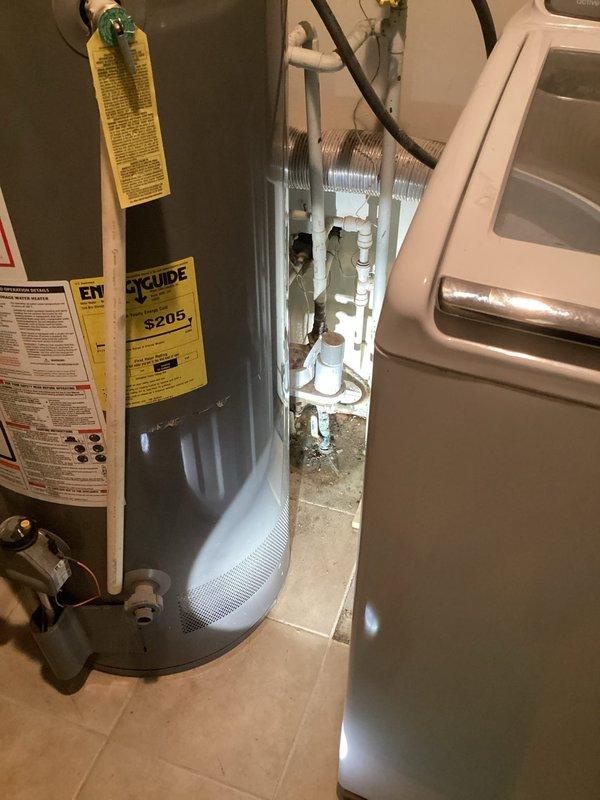 Responded to a reported water leak near the main shutoff and inspected the gas water heater, flexible water connectors, and adjacent supply piping in the utility area. Observed corrosion streaking on a vertical supply pipe near a flexible connector fitting, along with debris and staining at the base of the piping and a cramped clearance between the water heater and adjacent appliance. Documented conditions with photographs and noted the affected connection and supply line components for further evaluation and repair.