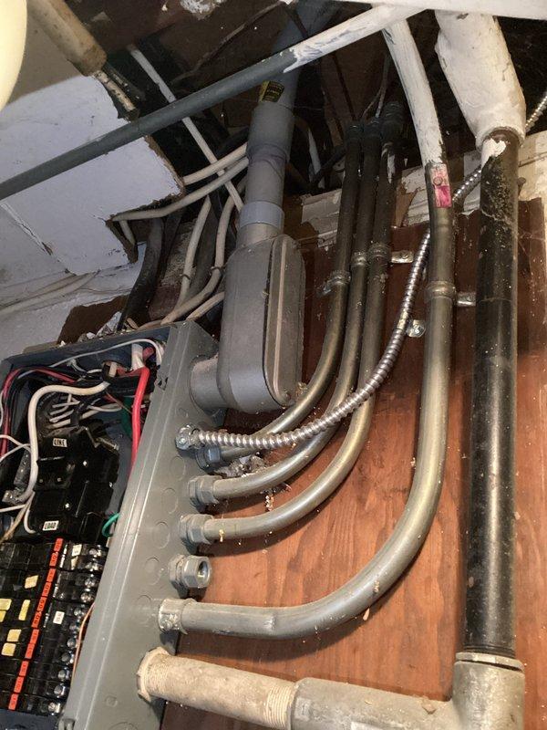 Completed electrical panel installation with proper conduit routing and connection. Multiple circuit breakers were installed with appropriate red, white, and black wiring, and all conduit pipes were properly secured to the wooden backing board with appropriate connectors and fittings.