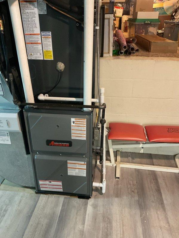 Identified and repaired a leaking PVC condensate drain line on a recently installed furnace system (5 months old). Inspected the T-connection junction where moisture damage was evident on the wooden flooring, and properly resealed the pipe joints to prevent further leakage from the vertical stacked HVAC units.