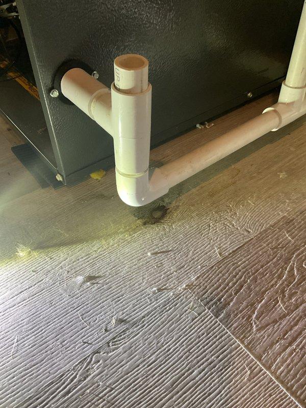 Identified and repaired a leaking PVC condensate drain line on a recently installed furnace system (5 months old). Inspected the T-connection junction where moisture damage was evident on the wooden flooring, and properly resealed the pipe joints to prevent further leakage from the vertical stacked HVAC units.
