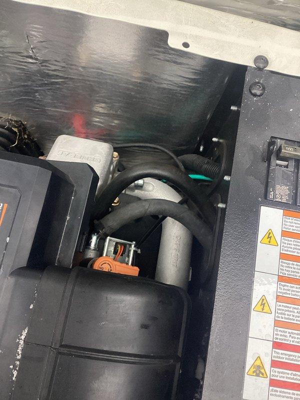 Performed warranty service on Generac unit. Inspected interior compartment including insulated walls, rubber hoses, and electrical components with warning labels. Examined battery installation and connections, noting NAPA ProForce battery with cable terminal attachment. Observed accumulation of dust and possible corrosion on housing components requiring cleaning.