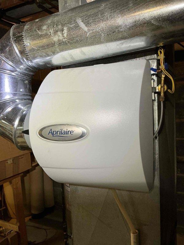 Performed heating maintenance service inspecting the Aprilaire whole-house humidifier installation. Noted water leakage from expansion tank with visible rust-colored staining on tank exterior. Recommended replacement of expansion tank to prevent further water damage to system components.