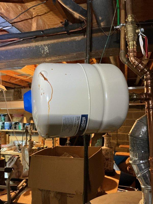 Performed heating maintenance service inspecting the Aprilaire whole-house humidifier installation. Noted water leakage from expansion tank with visible rust-colored staining on tank exterior. Recommended replacement of expansion tank to prevent further water damage to system components.