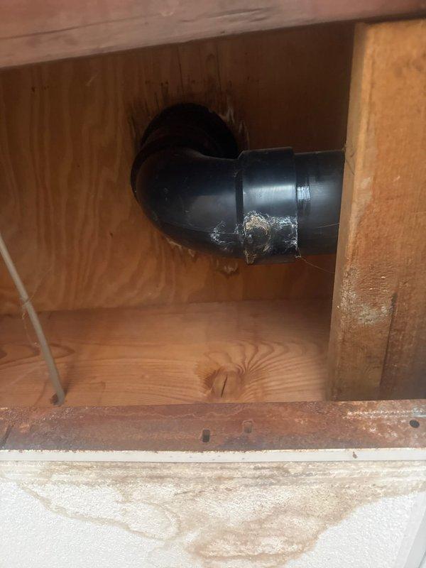 Performed maintenance inspection of water heater system and identified expansion tank requiring replacement. Assessed bathroom plumbing fixtures including toilet with assistive seat. Noted PVC drainage pipe with 90-degree elbow joint showing signs of deterioration at wall connection point with visible white residue. Recommended professional plumbing service for expansion tank replacement.