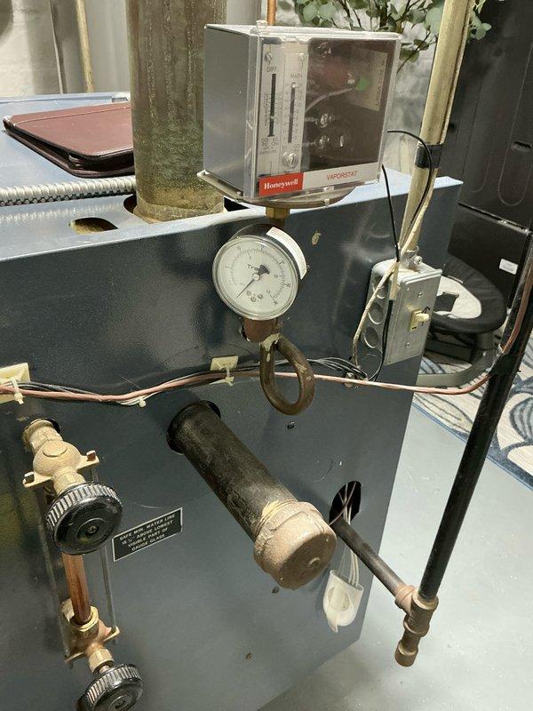 Inspected 23-year-old Weil-McLain EG/PEG-50 boiler (145k BTU/hr) with recurring pilot light issues requiring constant resetting. Observed significant corrosion at pipe connections, deteriorated insulation, and water damage at ceiling junction. Documented condition of Honeywell control system, pressure gauge, and associated valves for comprehensive replacement quote.