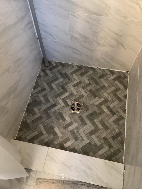 Responded to water leak complaint originating from upstairs bathroom affecting ceiling below. Inspected shower drain system where water was escaping; identified and repaired faulty shower drain seal in the marble-tiled enclosure with herringbone pattern floor.