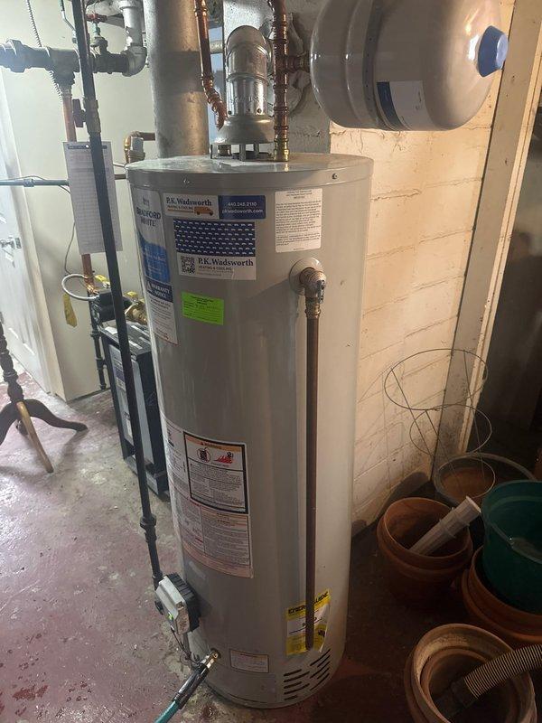 Completed installation of a new P.K. Wadsworth water heater in utility room, including proper connection of copper supply lines and ventilation piping. Installed black expansion tank above the unit and verified all plumbing connections for proper function and leak prevention.