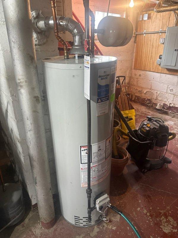 Completed installation of a new P.K. Wadsworth water heater in utility room, including proper connection of copper supply lines and ventilation piping. Installed black expansion tank above the unit and verified all plumbing connections for proper function and leak prevention.