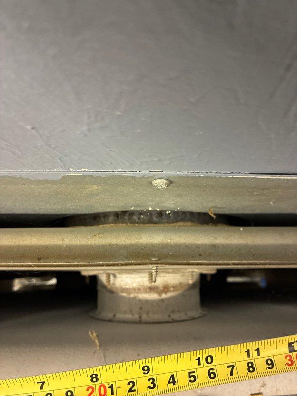 Conducted inspection of early 2000's garage heater unit for potential replacement options. Examined wall-mounted heating system with metal grille front and assessed connecting copper piping with valve. Measurements were taken of mounting components to determine appropriate replacement specifications.