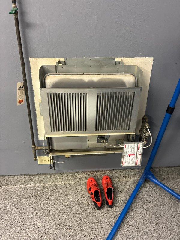 Conducted inspection of early 2000's garage heater unit for potential replacement options. Examined wall-mounted heating system with metal grille front and assessed connecting copper piping with valve. Measurements were taken of mounting components to determine appropriate replacement specifications.