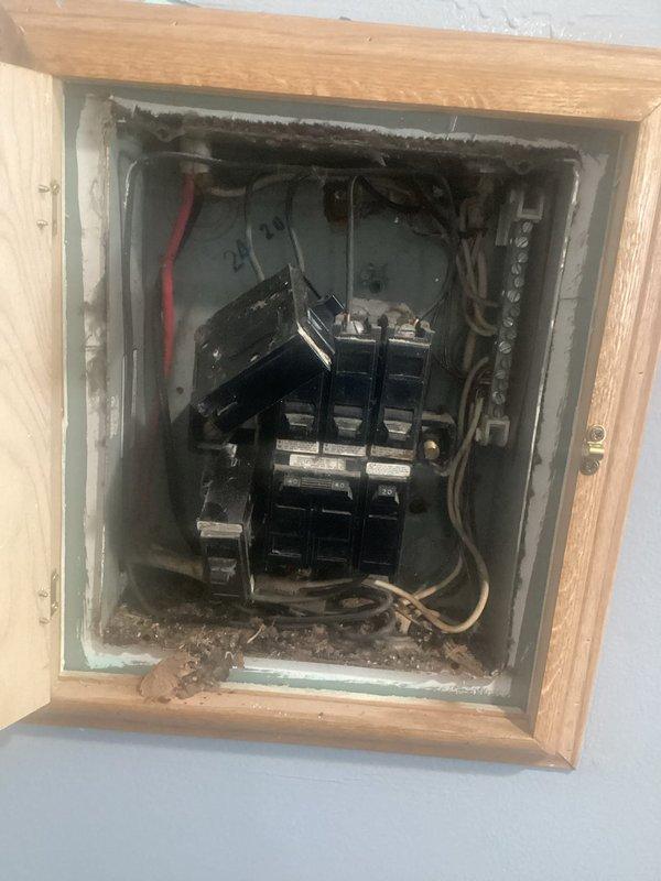 Conducted comprehensive assessment of existing electrical panel to provide customer with installation estimate. Panel appears to be an older model recessed into wall with wooden frame, showing signs of wear and accumulated dust. Observed multiple circuit breakers with various connected wiring including red and copper conductors that would need to be properly transferred during replacement.