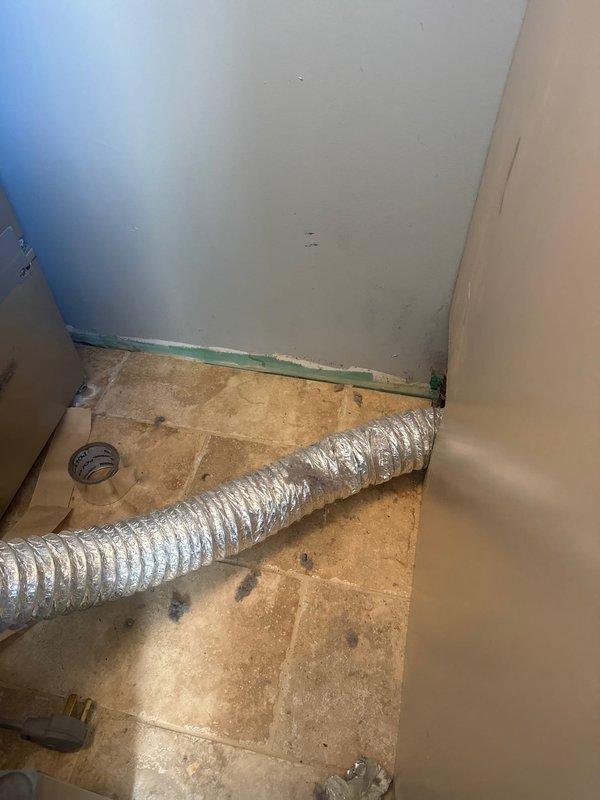 Inspected detached dryer vent ducting in utility area. Found flexible metallic duct disconnected from wall outlet. Reattached and secured aluminum duct to wall connection point, ensuring proper ventilation pathway was restored.