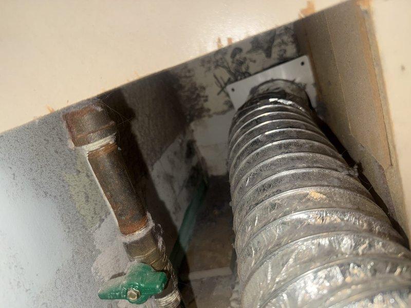 Inspected detached dryer vent ducting in utility area. Found flexible metallic duct disconnected from wall outlet. Reattached and secured aluminum duct to wall connection point, ensuring proper ventilation pathway was restored.
