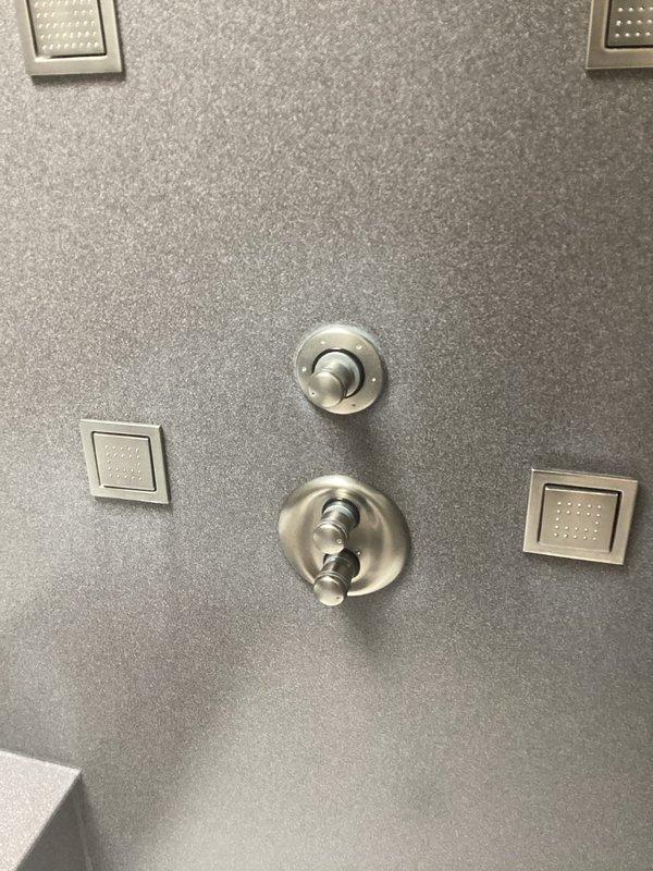 Replaced faulty Kohler shower mixing valve in bathroom renovation. Installed new valve assembly and verified proper hot/cold water mixing functionality. Final installation completed with brushed nickel trim kit on gray solid surface shower enclosure.