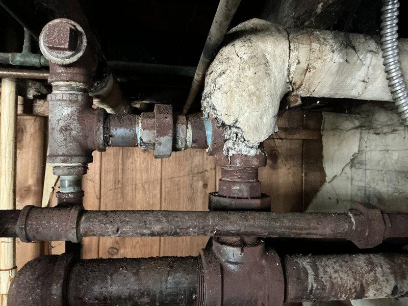 Conducted comprehensive assessment of aging boiler system for replacement estimate. Observed significant deterioration including extensive corrosion on iron distribution pipes, compromised pipe insulation, and multiple connection points showing advanced oxidation. System appears to be non-operational with visible red tag indicating potential safety concerns or previous service notification.