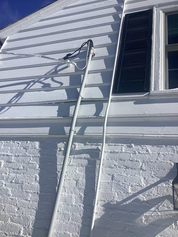 Secured loose conduit fasteners on exterior electrical installation per inspector requirements. Verified proper attachment of both metal electrical conduit and accompanying cable runs along white siding. Documentation photos confirm completed remediation.