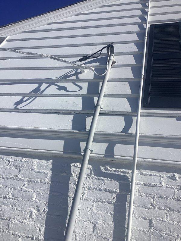 Secured loose conduit fasteners on exterior electrical installation per inspector requirements. Verified proper attachment of both metal electrical conduit and accompanying cable runs along white siding. Documentation photos confirm completed remediation.