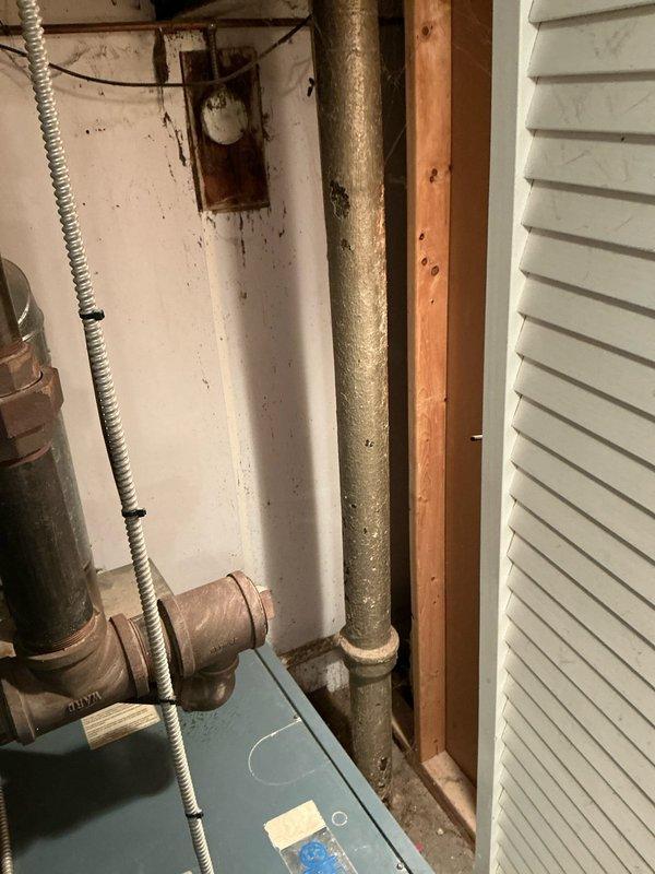 Performed assessment of aging boiler system showing significant corrosion on vertical piping and connection components. Unit inspection revealed a furnace/boiler with visible wear, mounted on deteriorating concrete pad, with panel access issues and compromised copper plumbing connections. Presented customer with replacement options based on evaluation findings.
