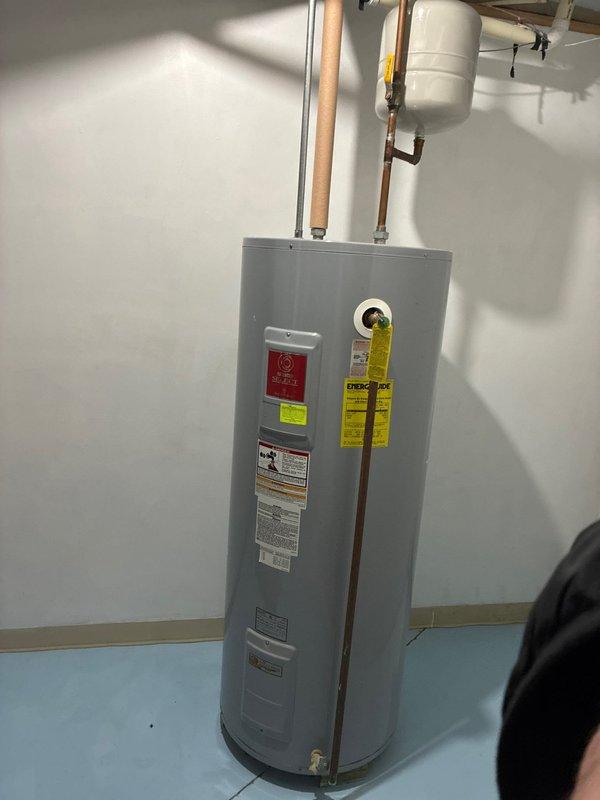 Conducted assessment for larger furnace replacement options. Current furnace shows significant aging with visible rust damage. Documented existing water heater installation and exterior conditions, noting substantial snow accumulation around the property that may impact installation logistics.