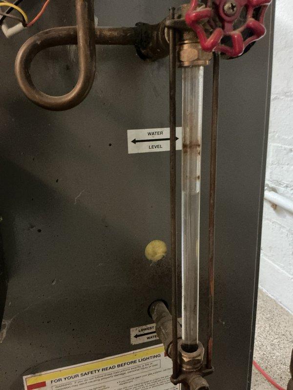 Performed comprehensive inspection of aging boiler system for new homeowner. Noted significant corrosion on control box and brass fittings, particularly at the Y-shaped valve assembly. Examined water level indicator tube and verified proper functioning of the red valve handle that controls water flow. System operational despite visible wear and oxidation on components.