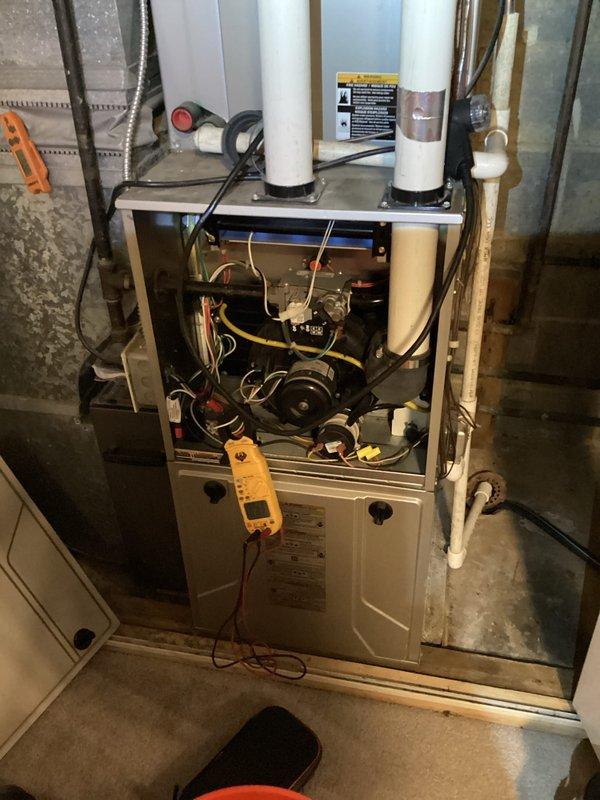 Performed monthly heating system maintenance on a furnace unit. Conducted electrical testing using multimeter to verify proper voltage and amperage readings (0.189A/0.083V). Inspected internal components with front panel removed, checking motor function and ventilation/drainage connections.