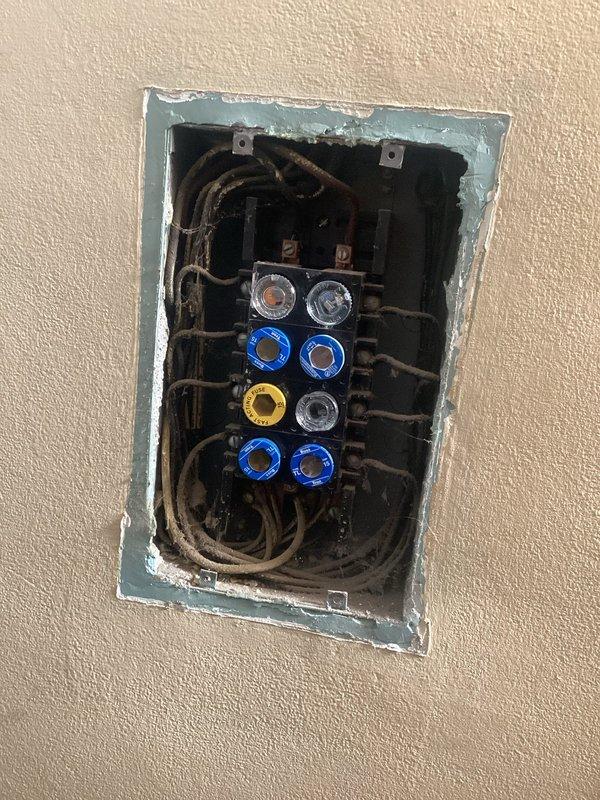 Conducted comprehensive inspection of outdated fuse panel system with multiple screw-in fuses showing signs of wear. Documented significant concerns including disorganized wiring, deteriorated insulation, and panel installation that fails to meet current electrical code requirements. Provided detailed estimate for complete home rewiring to address safety hazards and bring electrical system up to modern standards.