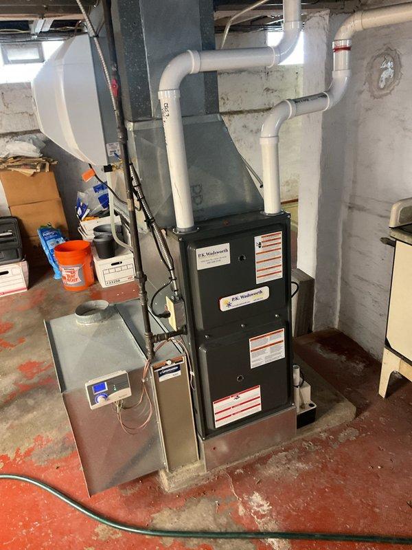 Performed routine heating maintenance on P.K. Wadsworth furnace system in basement utility room. Inspected and cleaned the filtration system, noting slight dust accumulation on the metal mesh filter. All ventilation components, including PVC exhaust pipes, were verified to be properly connected and functioning correctly.