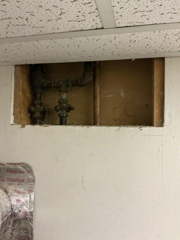 Conducted comprehensive assessment of existing plumbing infrastructure and ceiling access points to evaluate boiler replacement options. Inspected aging pipe connections and valve assemblies visible through wall access panel and ceiling opening. Photos documented current system configuration to support development of appropriate heating source alternatives.