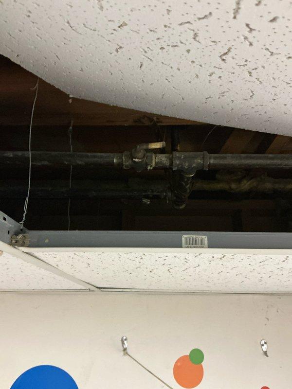 Conducted comprehensive assessment of existing plumbing infrastructure and ceiling access points to evaluate boiler replacement options. Inspected aging pipe connections and valve assemblies visible through wall access panel and ceiling opening. Photos documented current system configuration to support development of appropriate heating source alternatives.