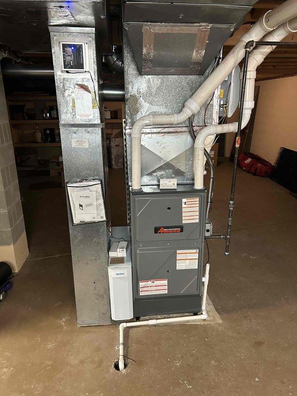 Successfully installed a complete 96% efficient Amana furnace system with integrated air conditioning and air scrubber in a basement utility area. System includes properly connected PVC ventilation pipes, sealed metal ductwork, and all required components mounted securely with appropriate clearances. Final inspection confirmed proper operation of all system components.