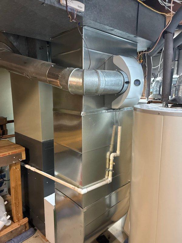 Successfully completed installation of a new furnace with complete metal ductwork system and proper PVC drainage piping. System includes a rectangular metal cabinet housing with round metal duct extending to the main air distribution network, positioned adjacent to the existing water heater in the utility area.