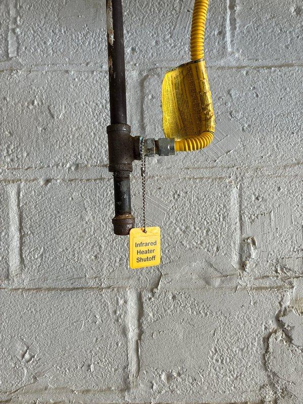 Conducted site assessment for replacement of non-operational garage heater. Inspected existing infrared heating system with dedicated gas line supply. Current installation includes black metal pipe with brass fitting and properly tagged shutoff valve connected to yellow corrugated gas line. Recommended replacement unit based on garage dimensions and existing utility connections.