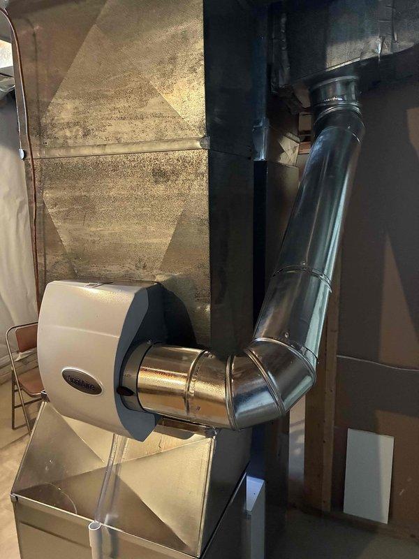 Successfully installed an Aprilaire 600 humidifier unit on the existing HVAC system, connecting it to the ductwork with proper metal piping and elbow joints. Mounted and configured the digital humidifier control panel, which is functioning correctly with current relative humidity reading at 23% and the "Humidifier On" indicator illuminated.