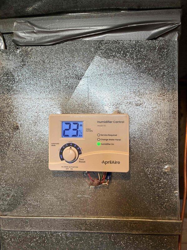 Successfully installed an Aprilaire 600 humidifier unit on the existing HVAC system, connecting it to the ductwork with proper metal piping and elbow joints. Mounted and configured the digital humidifier control panel, which is functioning correctly with current relative humidity reading at 23% and the "Humidifier On" indicator illuminated.