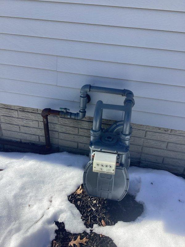 Completed site assessment for whole home generator installation. Documented existing electrical service meter setup and gas meter configuration to determine proper generator sizing and connection requirements. Current infrastructure includes standard residential electrical meter on wood backing board with dual conduit runs and an accessible gas meter with multiple pipe configurations that will require modification for generator fuel supply.