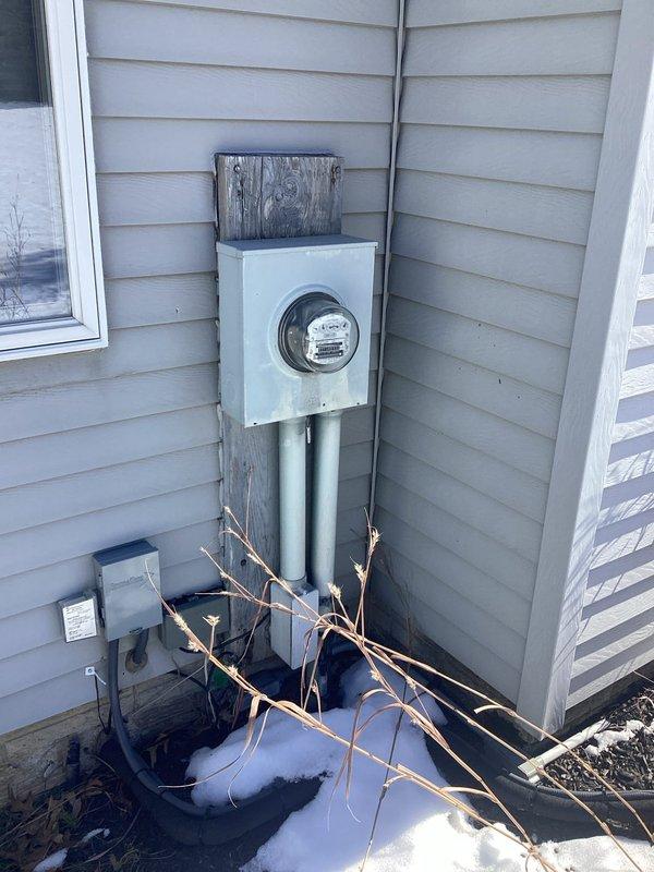 Completed site assessment for whole home generator installation. Documented existing electrical service meter setup and gas meter configuration to determine proper generator sizing and connection requirements. Current infrastructure includes standard residential electrical meter on wood backing board with dual conduit runs and an accessible gas meter with multiple pipe configurations that will require modification for generator fuel supply.