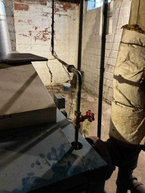 Conducted a site assessment for boiler replacement in a basement utility area with no current heat. Inspection revealed an outdated HVAC system with deteriorating components, including compromised gas line connections with green piping and brass fittings. Noted electrical concerns with exposed junction box and aging flex conduit that will require updating during replacement to meet current safety standards.