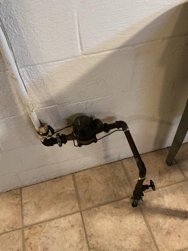 Conducted electrical inspection of wall receptacle and verified proper installation of outlet with connected load. Observed adjacent water meter and plumbing system during inspection, noting no electrical hazards present in utility area.