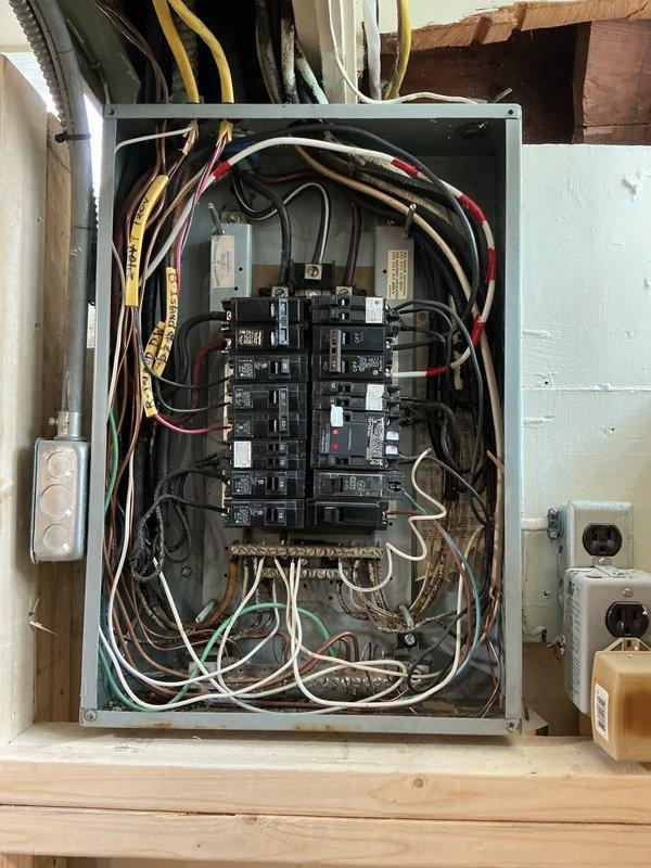 Performed electrical panel inspection and found disorganized wiring with multiple colored conductors (black, white, red, yellow, green) requiring proper organization. Identified and labeled all circuit breakers in the panel mounted on wooden wall structure, ensuring proper connections for safe operation and compliance with electrical code requirements.