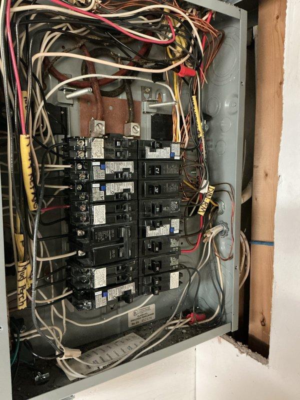 Performed electrical panel inspection and found disorganized wiring with multiple colored conductors (black, white, red, yellow, green) requiring proper organization. Identified and labeled all circuit breakers in the panel mounted on wooden wall structure, ensuring proper connections for safe operation and compliance with electrical code requirements.