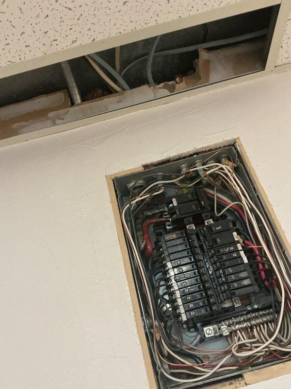 Performed comprehensive electrical panel inspection, documenting the condition of a dual-column circuit breaker panel with multiple numbered breakers (9-23). Observed bundled wiring configuration with white, red, and black conductors, noting some disorganization in wire routing but confirming functional operation of all components. Inspected ceiling access point above panel for proper conduit connections and structural integrity.