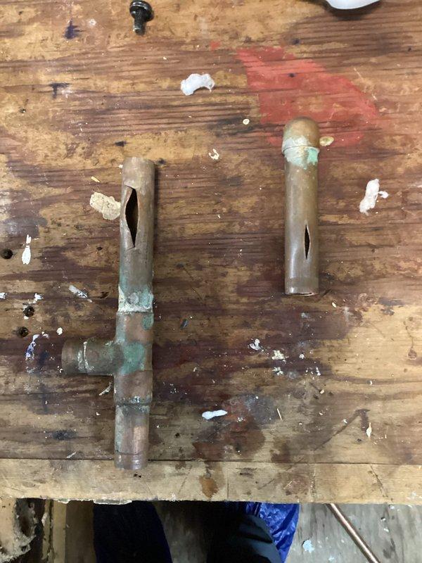 Responded to emergency call for burst pipe leaking into a closet area that was originally planned as a bathroom but never completed. Identified corroded copper T-fitting and straight pipe section with significant oxidation and verdigris formation at the joints as the source of the leak. Removed damaged components and replaced with new fittings, restoring proper function to the plumbing system and preventing further water damage to the property.