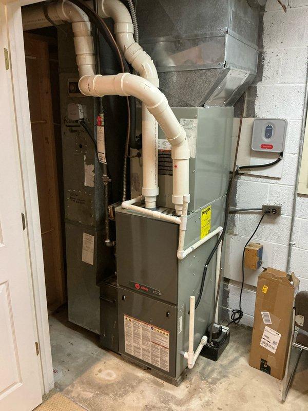 Conducted evaluation of aging forced air system and presented replacement options. Documented existing installation which includes a furnace unit with PVC exhaust/intake components, connected ductwork with transition piece, and electrical controls. System is mounted in concrete block utility room with proper ventilation configuration.