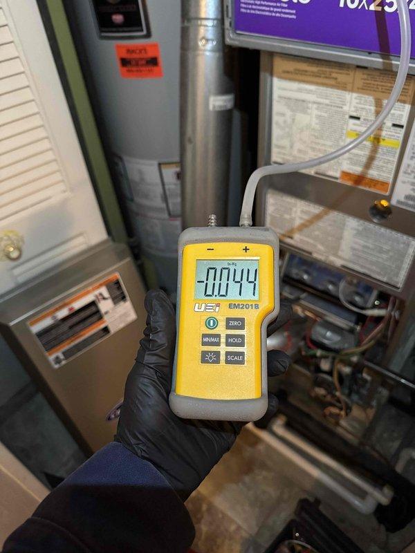 Completed scheduled heating maintenance on residential HVAC system. Performed combustion analysis on furnace with EM201B digital testing device, recording negative pressure readings of -0.044. Inspected adjacent Bradford White "Defender" water heater installation including ventilation ducts, supply lines, and gas connections, confirming proper setup and functionality.